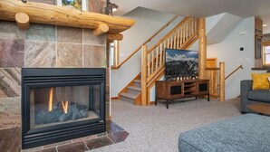 A living room with a fireplace, stone wall, wooden staircase, and a couch.