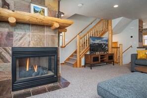 Un salon avec une cheminée, un mur en pierre, un escalier en bois et un canapé.