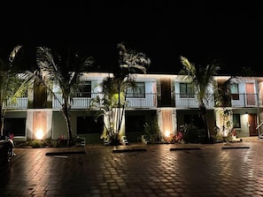 Un hotel de varios pisos con un patio empedrado, palmeras y una cascada decorativa.