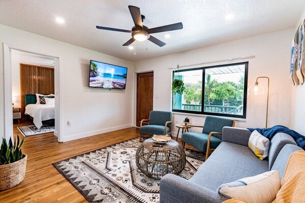 A modern living room with a ceiling fan, a large window with a view, a sofa, two armchairs, and a coffee table.