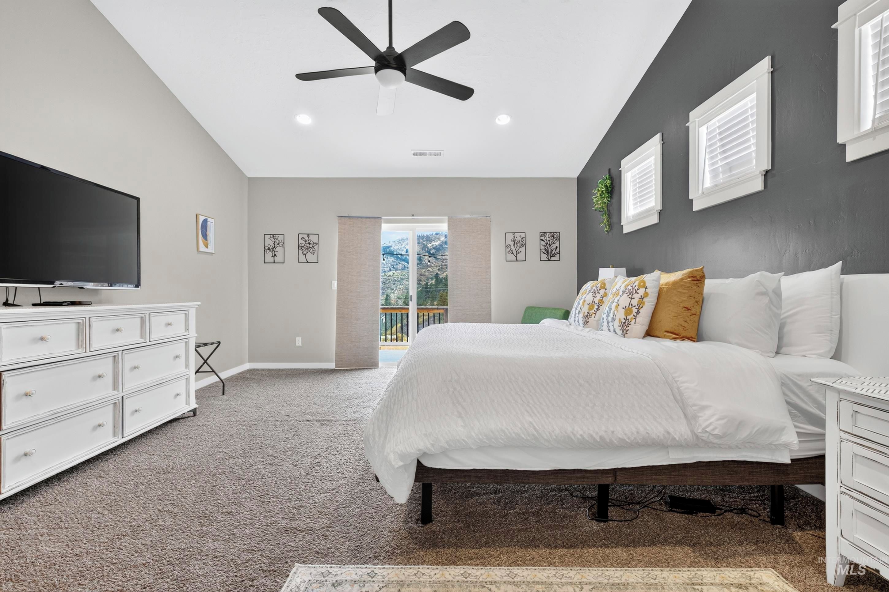 A bedroom with a bed, a TV, a ceiling fan, and a view through a door.
