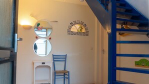 Une pièce avec un escalier bleu, une console blanche, une chaise bleue et deux miroirs fixés au mur.