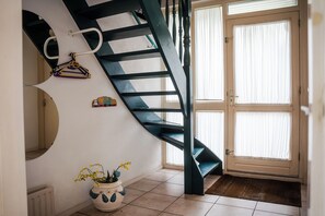 A spiral staircase with a dark finish, a potted plant with yellow flowers, and a door with white curtains.