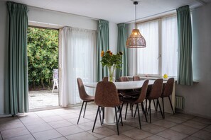A dining area with a round table, six chairs, and a hanging light fixture.