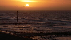 Un coucher de soleil sur l’océan, avec une jetée qui s’avance dans l’eau.