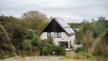 A modern house with a sloped roof, surrounded by dense greenery.