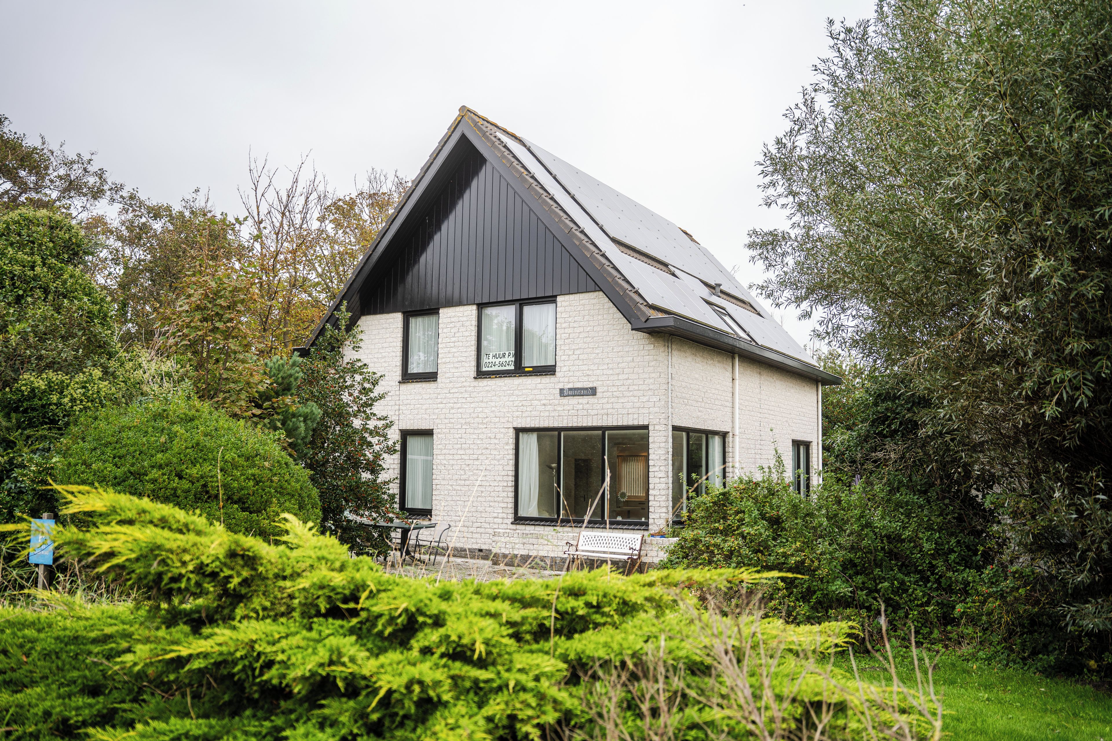 A two-story house with a sloped roof, large windows, and a visible outdoor seating area.