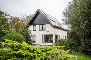 Ein zweigeschossiges Haus mit geneigtem Dach, großen Fenstern und einer sichtbaren Außenbereich-Sitzgelegenheit.