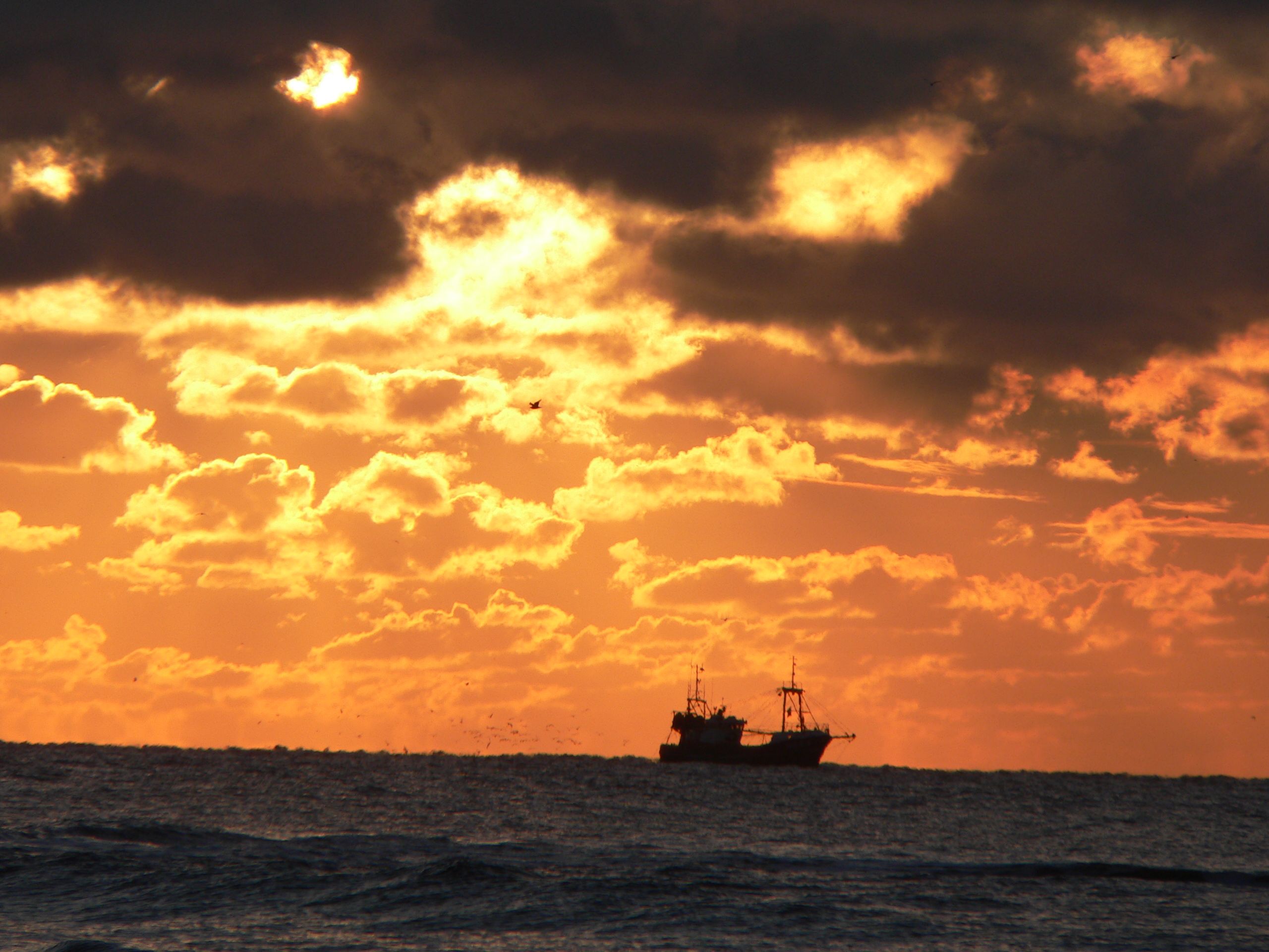 A ship on the water during sunset with clouds in the sky.