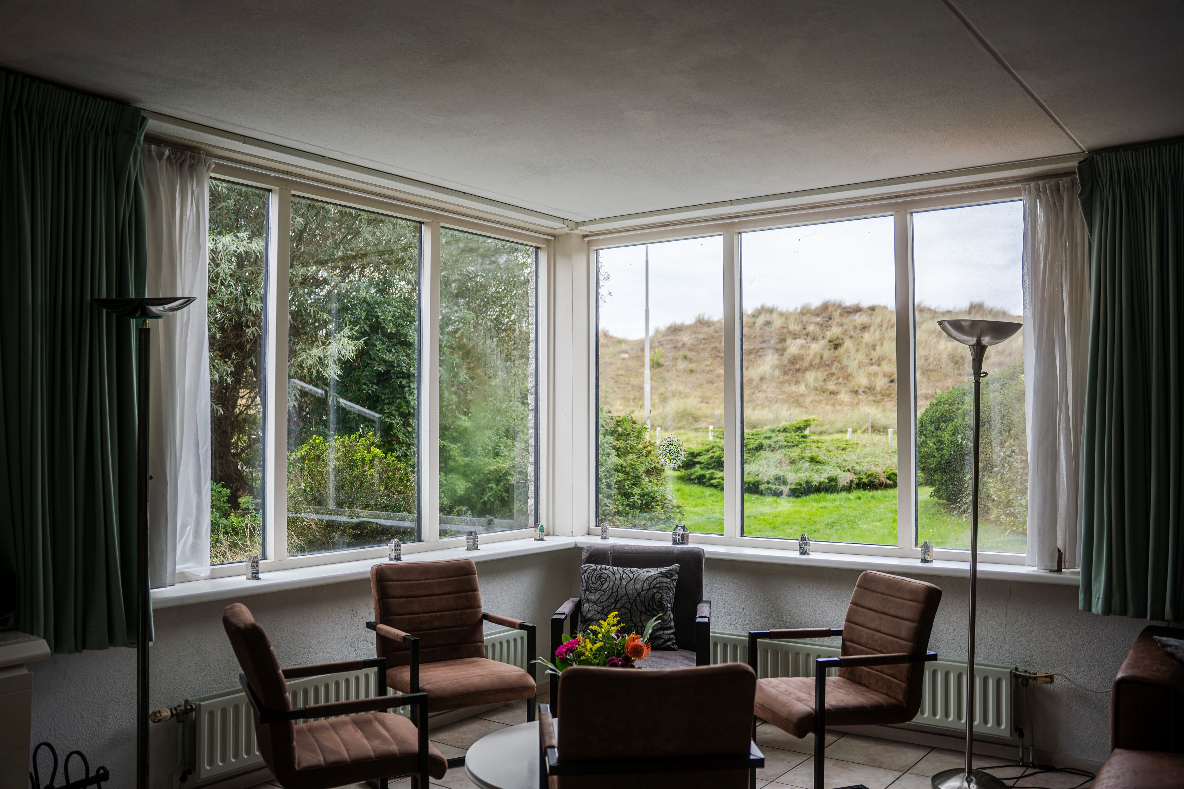 A room with a bay window, two chairs, a table, and a floor lamp.