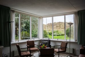 A room with a bay window, two chairs, a table, and a floor lamp.