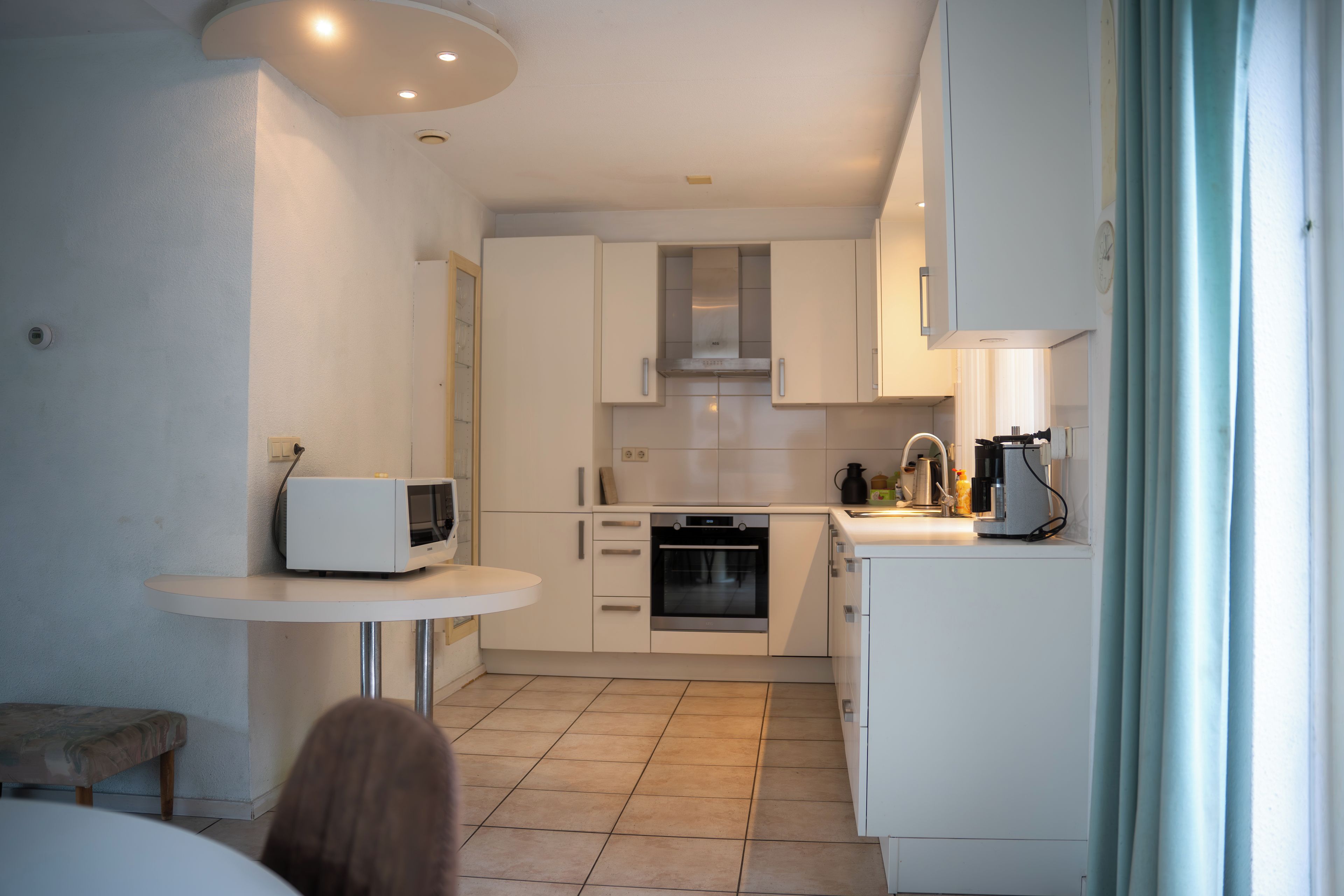 A compact kitchen with white cabinets, a microwave, an oven, and a small dining area with a table and bench.