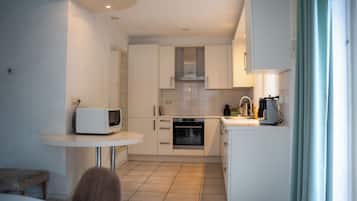 A compact kitchen with white cabinets, a microwave, an oven, and a small dining area with a table and bench.