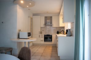 A compact kitchen with white cabinets, a microwave, an oven, and a small dining area with a table and bench.