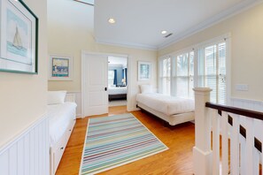 Two beds with white bedding, a colorful area rug, and a window with blinds.
