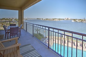 Een balkon met rieten meubilair, uitzicht op een waterpartij en een zwembad.