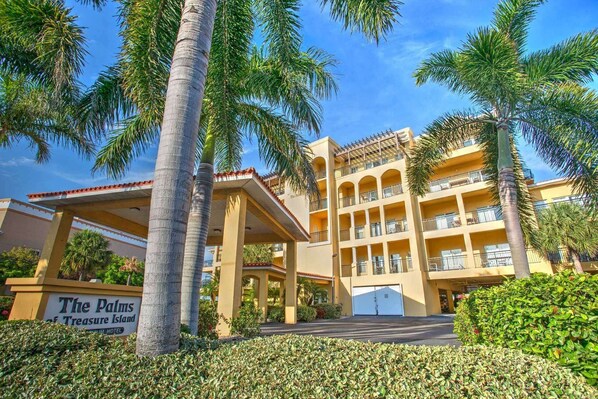 A hotel with a covered entrance, palm trees, and a sign reading "The Palms of Treasure Island".