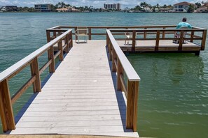 A wooden pier leading to a dock with a view of the water and buildings in the background.