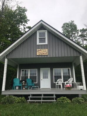 Een gebouw met twee verdiepingen, een veranda en twee groene Adirondack-stoelen op de veranda. Een bord met de tekst 'Rose Cottage'.