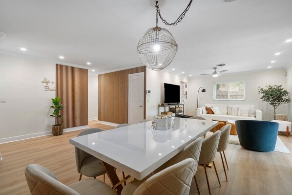 A modern living room with a white sofa, a blue armchair, and a dining area with a white table and chairs. - Chic Coastal - Heated Pool at Request, Near PGA & Everything! (Palm Beach Gardens)