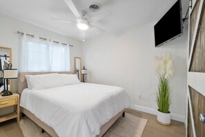 A bedroom with a bed, a ceiling fan, a TV mounted on the wall, and a potted plant. - Chic Coastal - Heated Pool at Request, Near PGA & Everything! (Palm Beach Gardens)