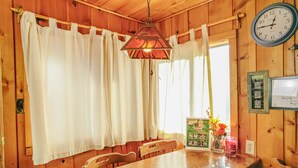 A wooden dining room with a table, chairs, a hanging light fixture, and a wall clock. - Original RMNP Riverfront Cabin on the Thompson River (Estes Park)