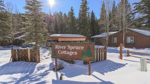 A sign for River Spruce Cottages with a wooden fence and snow-covered ground. - Original RMNP Riverfront Cabin on the Thompson River (Estes Park)