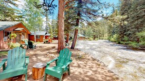 A cabin with a wooden deck, two green Adirondack chairs, and a picnic table. - Original RMNP Riverfront Cabin on the Thompson River (Estes Park)