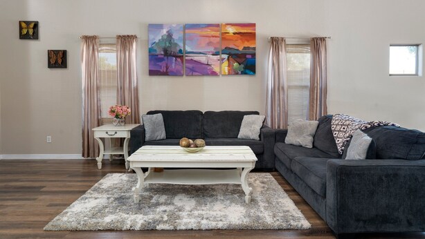 A living room with a dark grey sofa, a white coffee table with decorative items, a beige rug, and a large abstract painting on the wall. - Phx Escape CENTRAL family pet friendly 4 bd sleeps 10 (Phoenix)