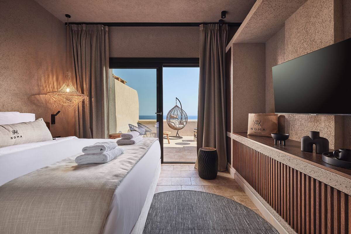 A hotel room with a bed, a TV, a desk, and a view of the sea.