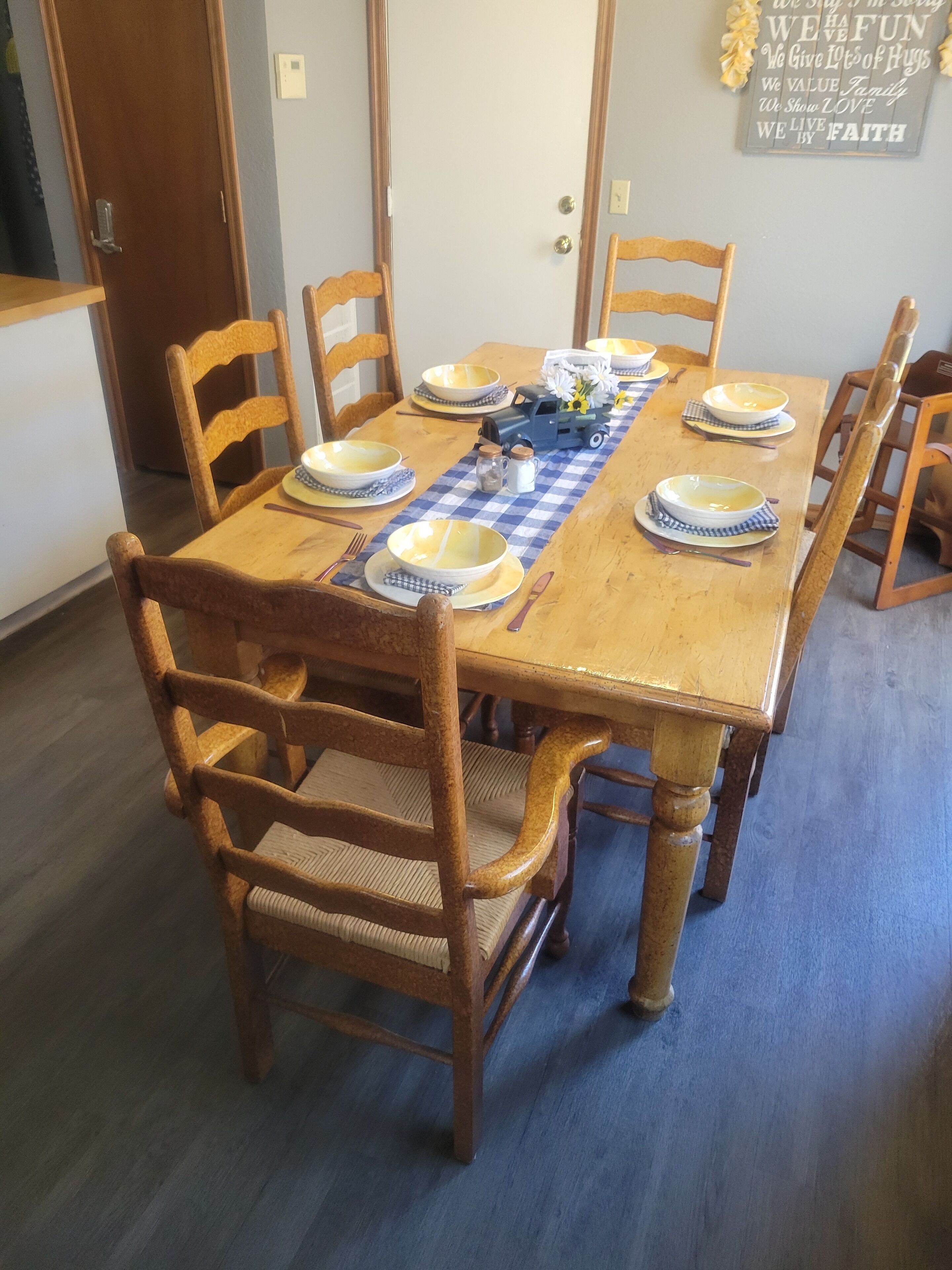 A dining table set for six with wooden chairs, a blue and white checkered tablecloth, and a decorative truck centerpiece.