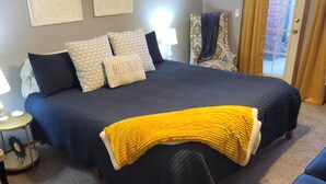Quarto com cama grande, mesa de cabeceira, abajur e uma cadeira.