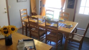 Uma sala de jantar com uma mesa e cadeiras de madeira, um lustre e uma janela com cortinas.
