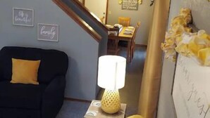 Uma sala de estar com um sofá, uma luminária e uma área de jantar ao fundo.