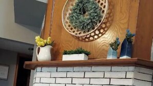 Uma lareira com revestimento de tijolos brancos, uma grinalda decorativa acima e uma pequena planta na mantega.