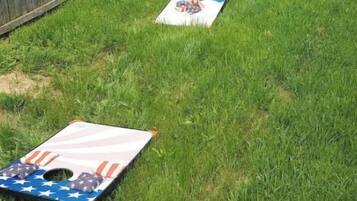 A grassy backyard with a wooden fence, a small play structure, and a mat with an American flag design.