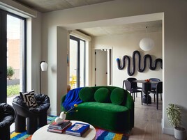 Una sala de estar moderna con un sofá verde, sillones negros y una zona de comedor con una mesa y sillas.
