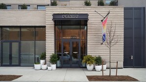 A modern building with a large entrance, potted plants, and a flag. - Penny Williamsburg (Brooklyn)