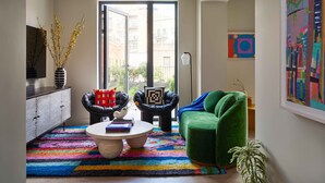 A modern living room with a green sofa, two armchairs, a coffee table, and a colorful rug. - Penny Williamsburg (Brooklyn)