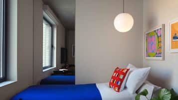 Une chambre d’hôtel avec deux lits, une grande fenêtre, un luminaire suspendu et un mur orné d’œuvres d’art colorées.