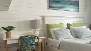 Un dormitorio con cama, escritorio, silla, lámpara, planta y un cuadro en la pared.