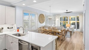 A modern kitchen with a central island, white cabinetry, and a dining area with a wooden table and chairs. - Adagio - “Sea View Serenity” - Beautifully Redesigned 3 BR Unit Overlooking The Pool! (Santa Rosa Beach)