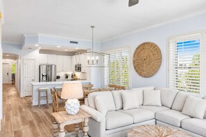 A modern kitchen with white cabinetry, a central island, and a dining area with a white sofa and wooden chairs. - Sea View Serenity - 3BR/3BA Adagio Condo - Sleeps 8 - Community Pool View (Santa Rosa Beach)