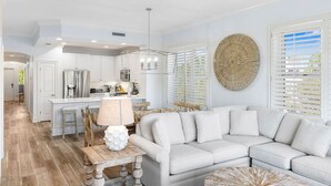 A modern kitchen with white cabinetry, a central island, and a dining area with a wooden table and chairs. - Adagio - “Sea View Serenity” - Beautifully Redesigned 3 BR Unit Overlooking The Pool! (Santa Rosa Beach)