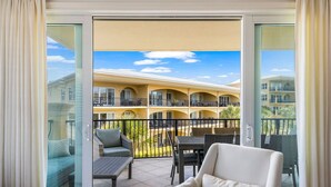 A balcony with outdoor furniture, a glass door, and a view of a building with balconies. - Adagio - “Sea View Serenity” - Beautifully Redesigned 3 BR Unit Overlooking The Pool! (Santa Rosa Beach)