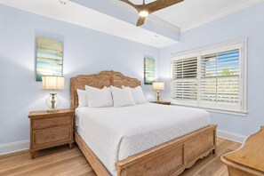 Une chambre à coucher avec un lit en bois, des tables de chevet, un ventilateur de plafond et une fenêtre avec des stores.