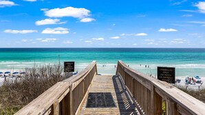 A wooden boardwalk leading to a beach with clear blue water and a few people in the distance. - Adagio - “Sea View Serenity” - Beautifully Redesigned 3 BR Unit Overlooking The Pool! (Santa Rosa Beach)