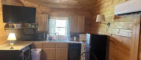 A compact kitchen with wooden walls and ceiling, a microwave, stove, sink, and a dining area with a table and chairs.