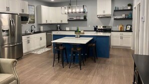 A modern kitchen with white cabinets, a central island with stools, stainless steel appliances, and a pendant light.