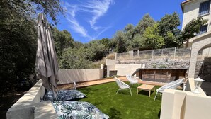A well-maintained outdoor patio with artificial grass, white wicker furniture, and a stone wall. - Villa Avec Piscine en Plein Coeur de Bastia (Bastia)